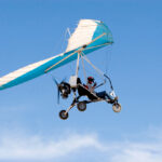 Osoba pilotujúca motorový závesný klzák počas letu na modrej oblohe – dokonalý darček pre adrenalínových nadšencov.